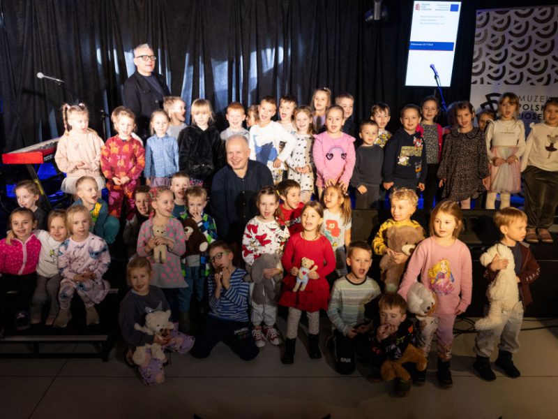 Grupa ludzi w sali kinowej muzeum. Dzieci uczestniczące w zajęciach z gwiazdą Piotrem Wojtasikiem