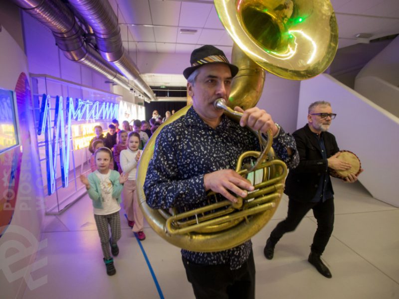 Piotr Wróbel grający na puzonie w czasie zajęć Małej Akademii Instrumentów, w tle dzieci i gospodarz muzyczny Miłosz Wośko