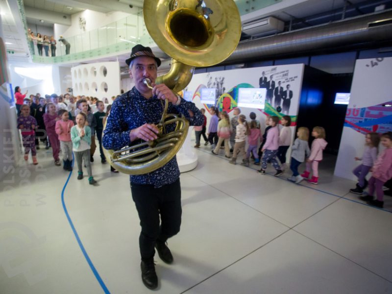 Piotr Wróbel grający na puzonie w czasie zajęć Małej Akademii Instrumentów, w tle dzieci uczestniczące w zajęciach