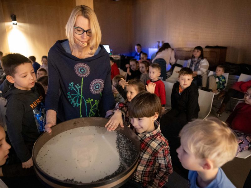 Grupa dzieci przy bębnach z artystką w sali muzeum, na zajęciach pt