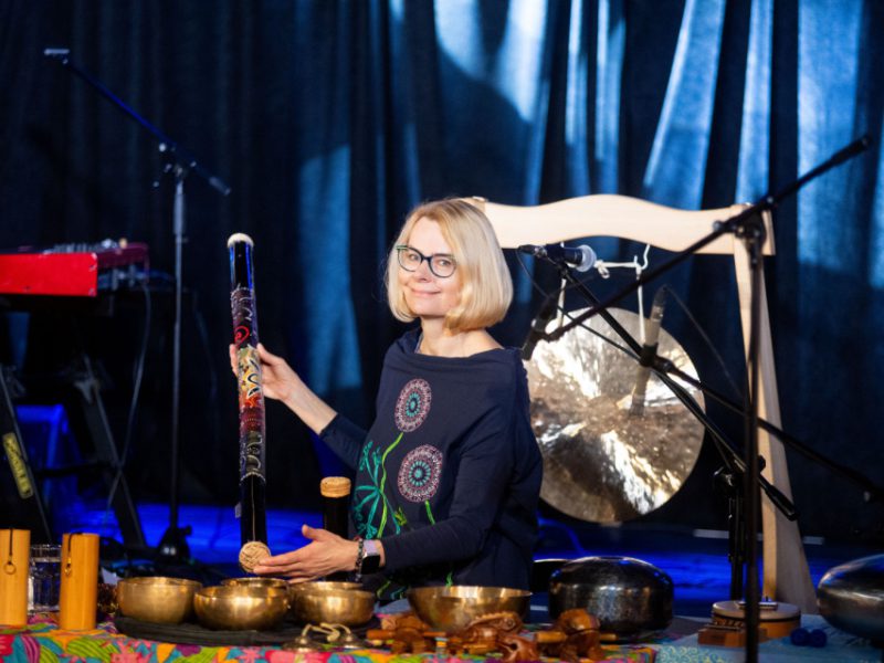 Artystka prezentująca instrumenty, w tle grupa dzieci uczestniczących w zajęciach
