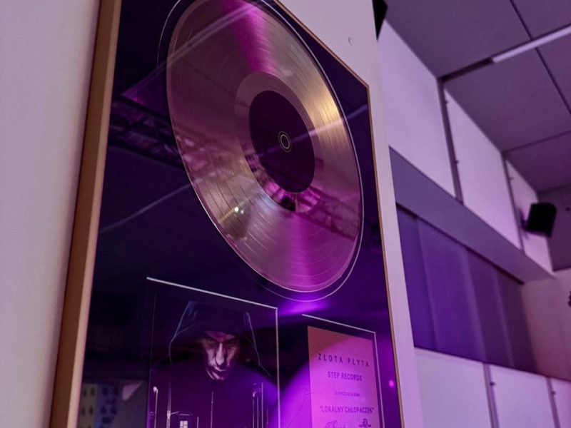 Zbliżenie na złotą płytę w gablocie na ścianie muzeum. Poniżej płyty okładka albumu „Lokalny Chłopaczek” rapera Intruz z wizerunkiem mężczyzny w czarnej bluzie z kapturem. Obok tabliczka z napisem „Złota Płyta – Step Records” z podpisami i logotypami wydawcy