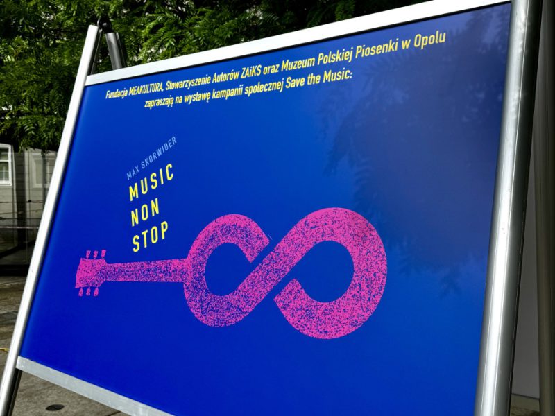 Plakat z tytułem „Music Non Stop” na ciemnoniebieskim tle. Pośrodku znajduje się różowa grafika w kształcie gitary, której pudło rezonansowe przechodzi w znak nieskończoności