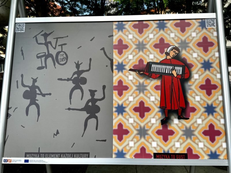 Plansza wystawowa z dwoma ilustracjami. Po lewej stronie postać w czerwonym turbanie grająca na flecie przed wijącym się wężem, z podpisem „MUZYKA TO RYTUAŁ”. Po prawej czarnoskóry mężczyzna z różową opaską na głowie, grający na jaskrawo kolorowej gitarze w kształcie żyrafy, z podpisem „MUZYKA TO ZABAWA”